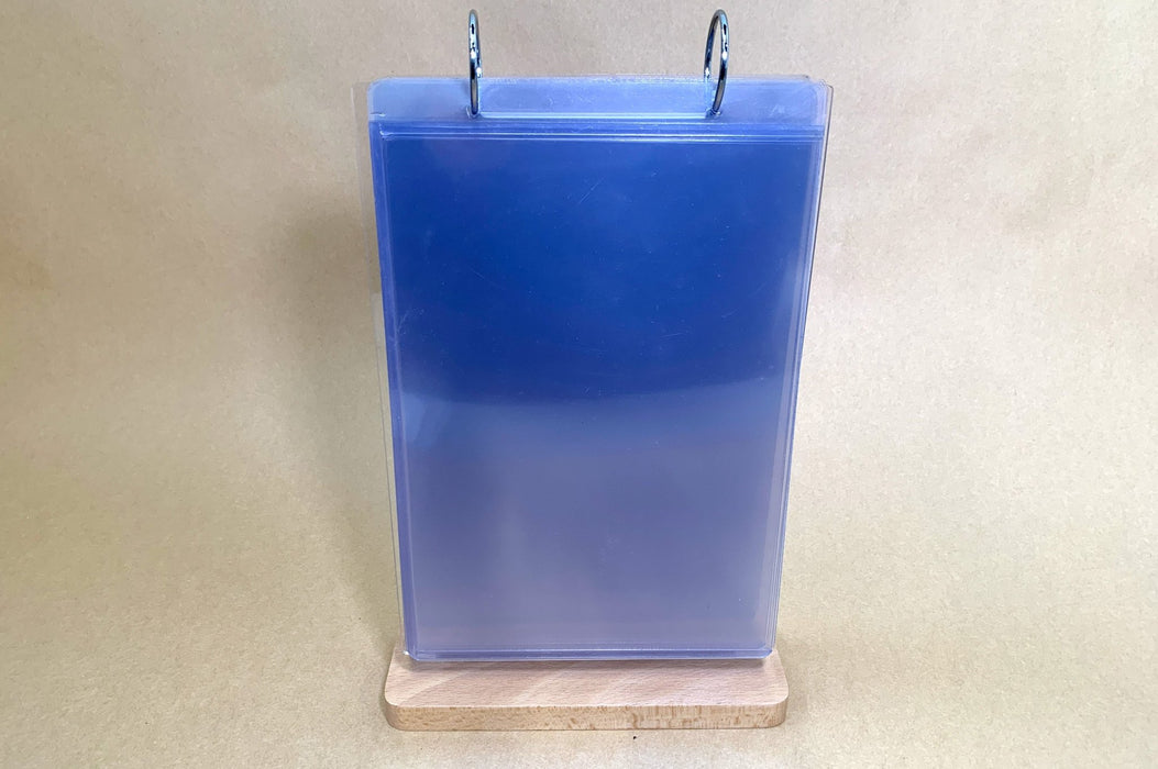 Front view of a tabletop flip menu stand showing clear 4x5.9 inch display pockets held by metal binder rings on a wooden base