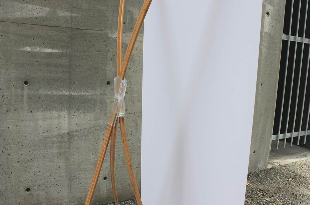 Side angle view of a bamboo X-stand display showing the blank white reverse side of the vinyl banner attached to natural bamboo support arms