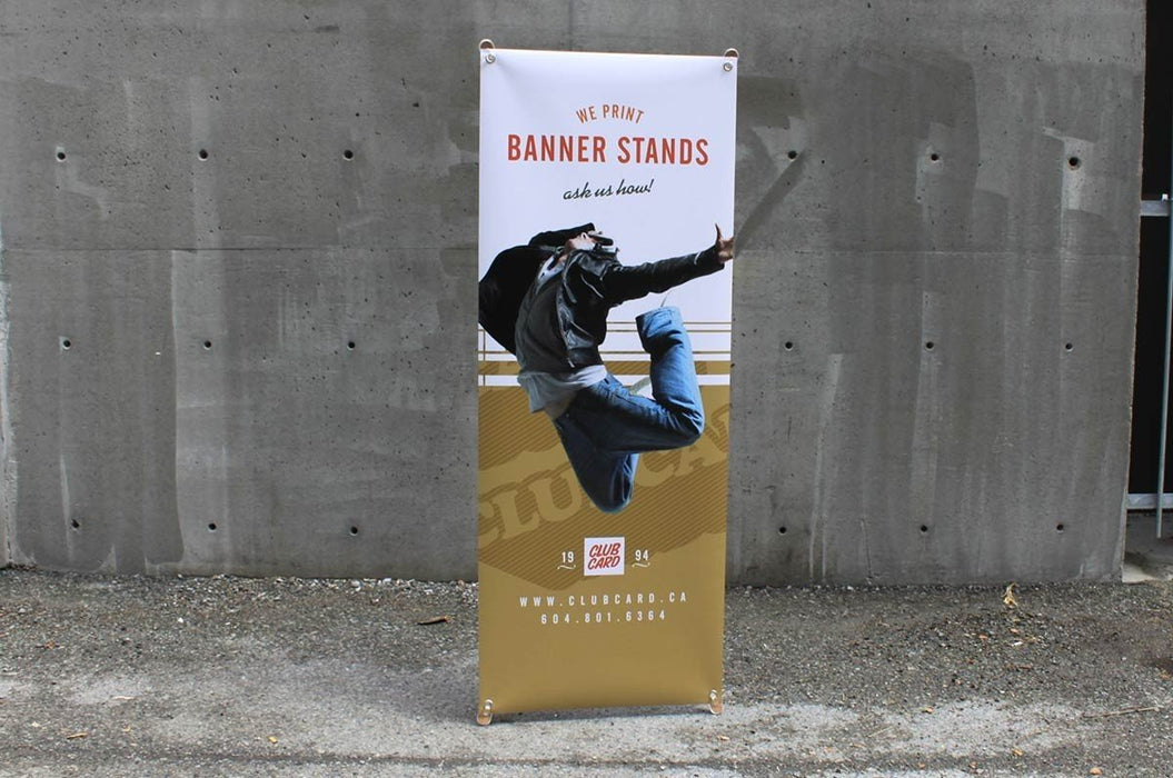 Eco-friendly bamboo x-stand banner display featuring custom printed graphic "WE PRINT BANNER STANDS ask us how!" set outdoors against a concrete wall.
