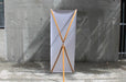 Rear view of a bamboo X-stand banner display showing the X-frame bamboo leg structure, center hub, and back support leg against a concrete wall.