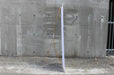 Side profile view of a bamboo X-stand display showing the flexible bamboo support arms hooked to the vertical white banner against a concrete wall.