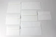 Grid arrangement of blank white wove envelopes in various standard card and letter sizes displayed on a light surface.