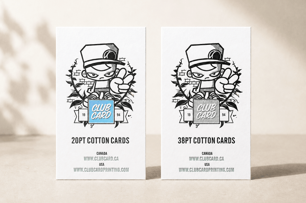 side-by-side comparison of 20pt and 38pt cotton letterpress business cards featuring Clubcard Vancouver's peace man mascot, with the 20pt card on the left featuring a blind debossed logo over a metallic blue foil square and the 38pt card on the right featuring a blind debossed logo over an iridescent foil square, printed by Clubcard Vancouver