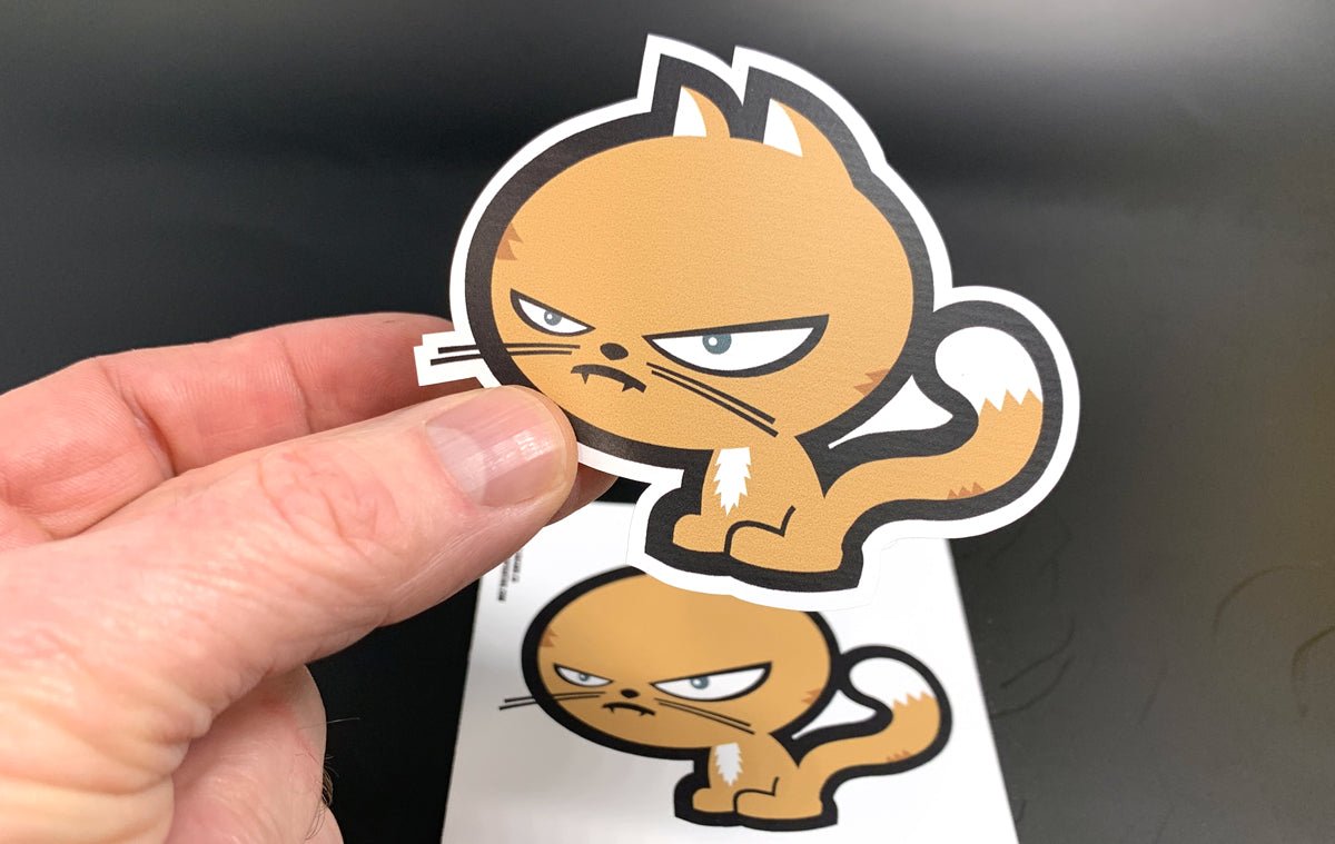 Hand peeling a custom shape vinyl sticker sample featuring Clubcard Vancouver's orange grumpy cat mascot character illustration, printed by Clubcard Vancouver