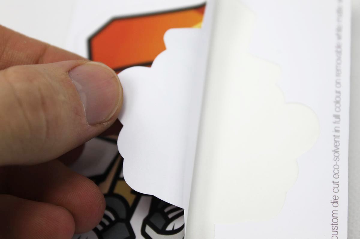 Hand peeling the paper backing off a custom shape vinyl sticker sample showing the adhesive layer, printed by Clubcard Vancouver