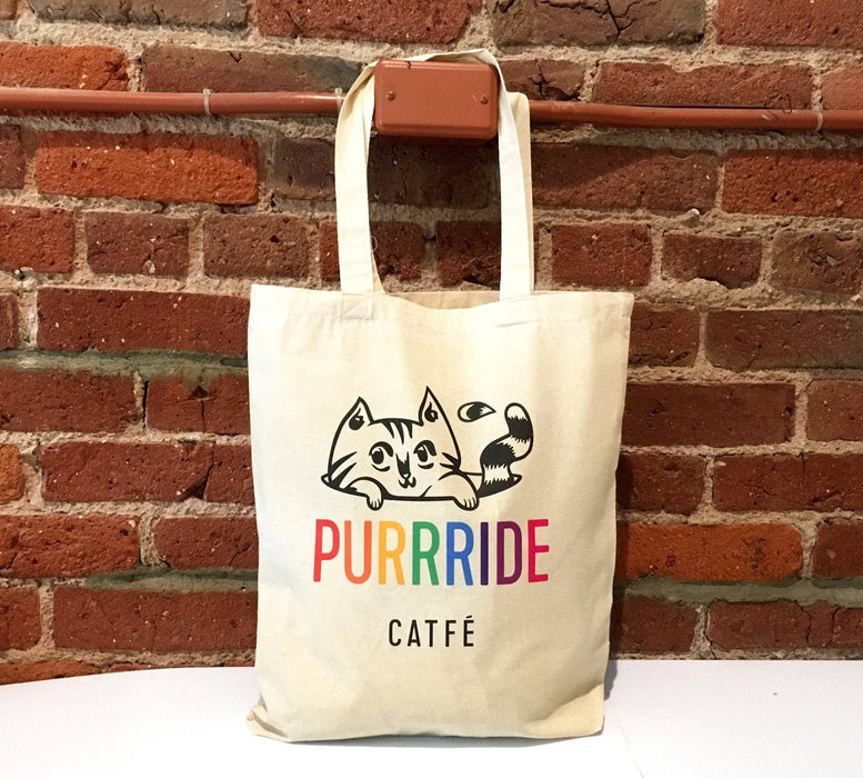 Custom printed natural cotton tote bag sample featuring the Purrride Catfé logo against a red brick wall background, printed by Clubcard Vancouver