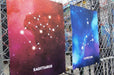 Two large fine art print samples displayed on a chain-link fence featuring Sagittarius and Capricorn zodiac constellation illustrations in vibrant galaxy art, printed by Clubcard