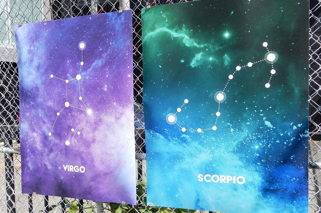 Two large fine art print samples displayed on a chain-link fence featuring Virgo and Scorpio zodiac constellation illustrations in vibrant galaxy art, printed by Clubcard Vancouver