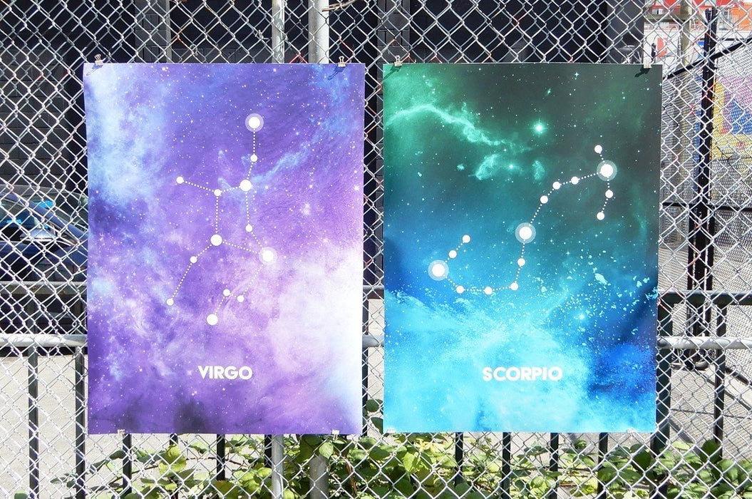 Two large fine art print samples displayed on a chain-link fence featuring Virgo and Scorpio zodiac constellation illustrations in vibrant galaxy art, printed by Clubcard Vancouver