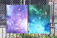 Two large fine art print samples displayed on a chain-link fence featuring Virgo and Scorpio zodiac constellation illustrations in vibrant galaxy art, printed by Clubcard Vancouver