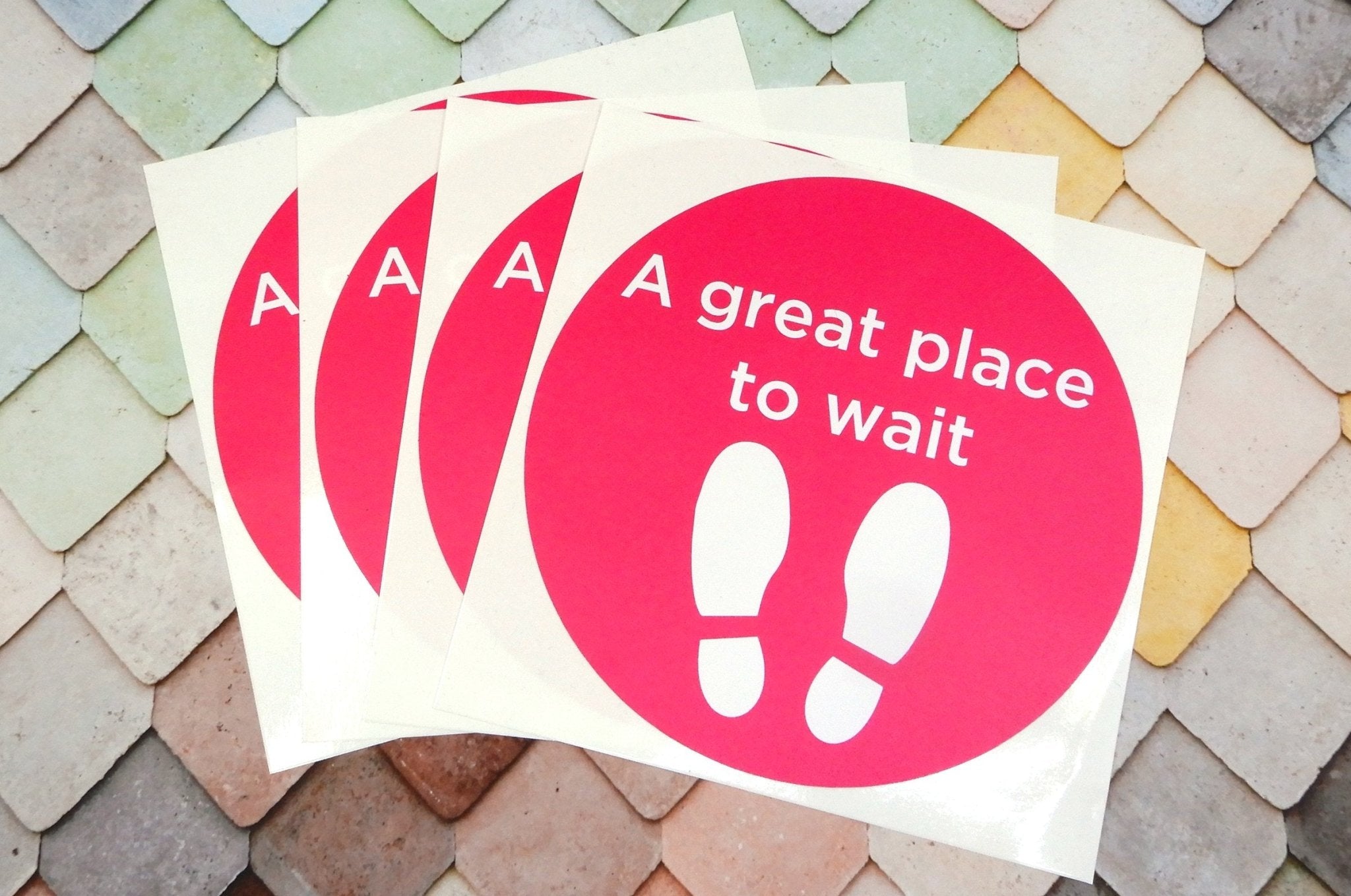 Fanned-out stack of custom white square vinyl sheets printed with bright pink oval floor stickers reading 
