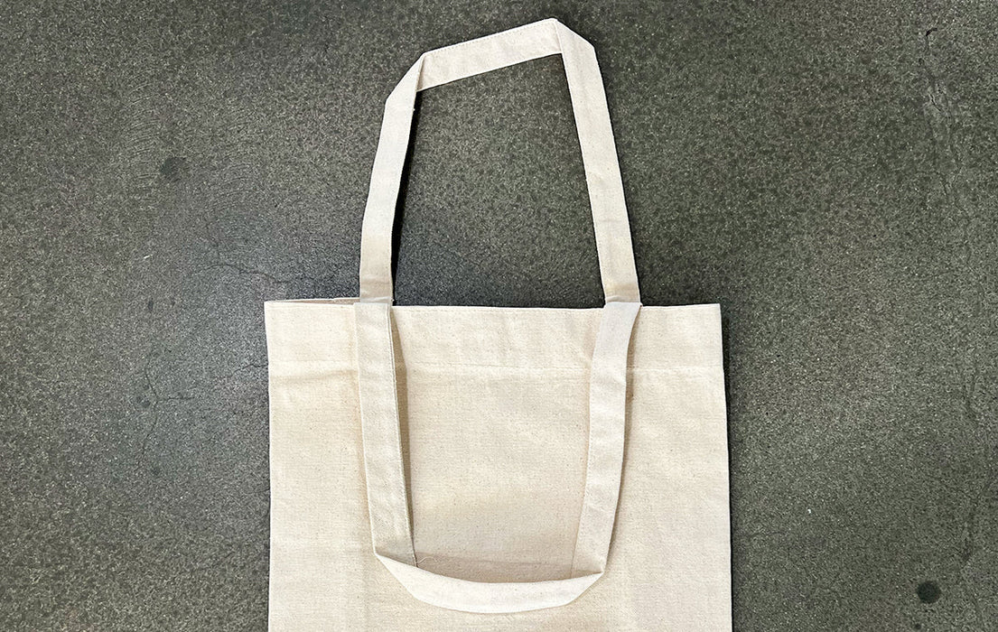 Unprinted natural heavyweight recycled cotton canvas tote bag lying flat on a grey surface - Clubcard Vancouver