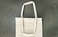 Unprinted natural heavyweight recycled cotton canvas tote bag lying flat on a grey surface - Clubcard Vancouver