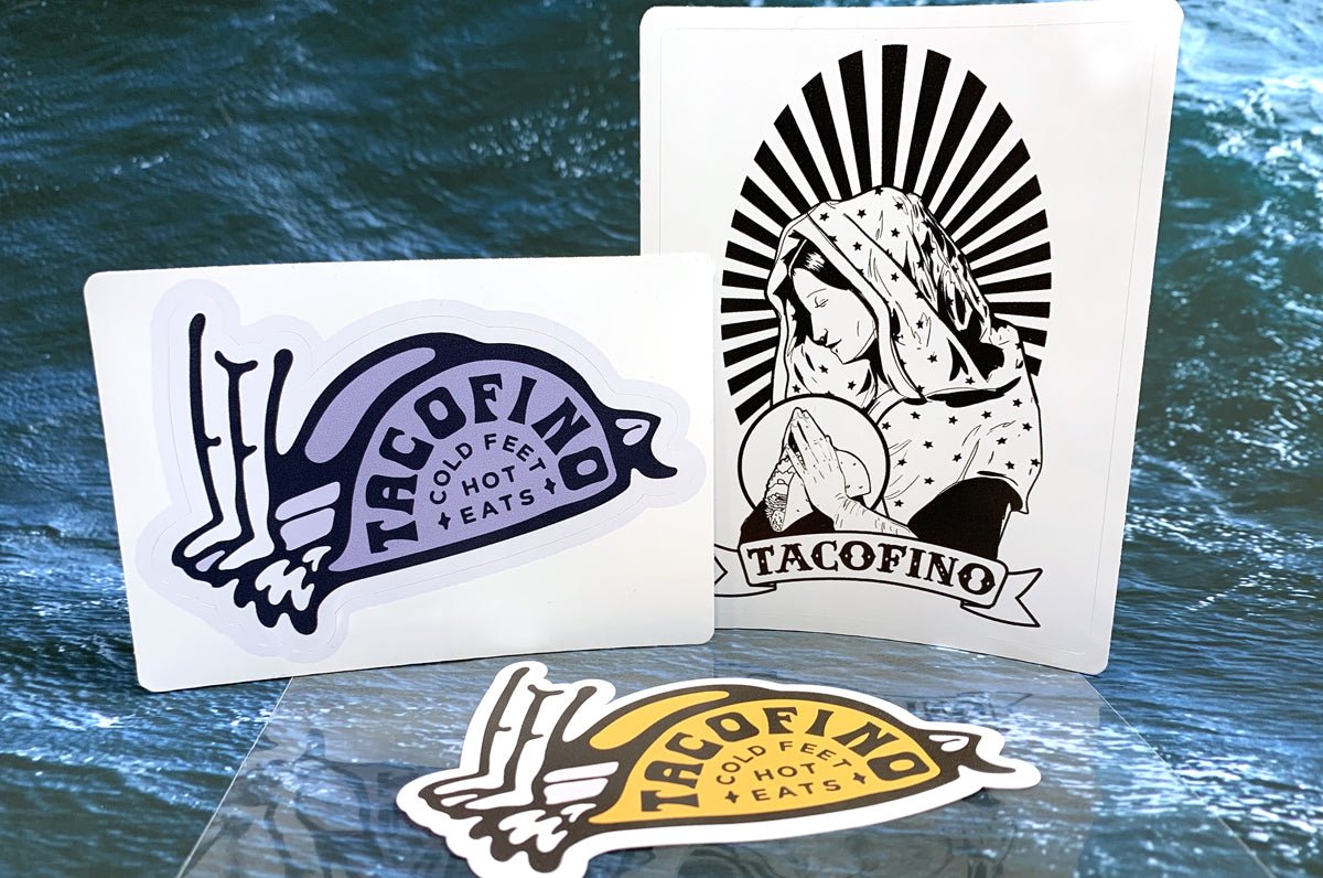 Custom shape vinyl sticker samples featuring black and yellow Tacofino logo graphics on a blue ocean background, printed by Clubcard Vancouver