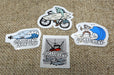 Custom shape vinyl sticker samples featuring Ucluelet and Tofino coastal lifestyle illustrations on a burlap background, printed by Clubcard Vancouver