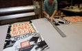 Print shop technician using a ruler and utility knife to trim printed Boxing Week Sale replacement banners