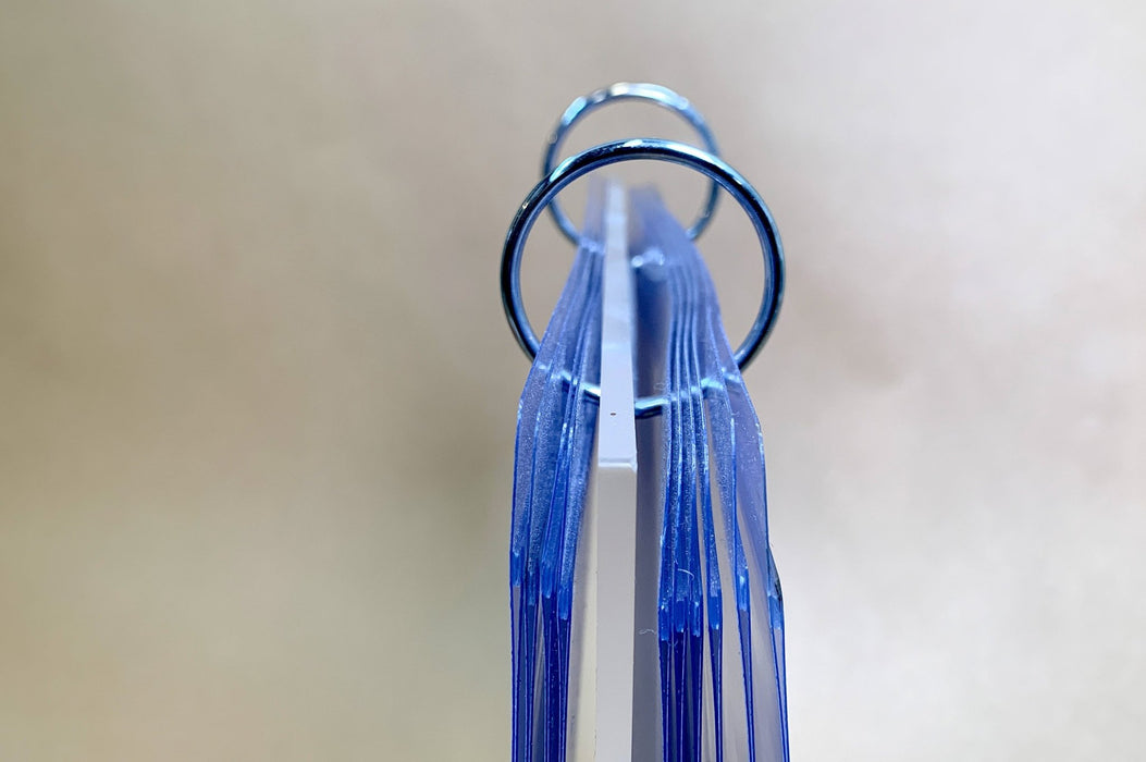 Top-angle close-up view of metal binder rings holding clear display pockets with protective film on a tabletop acrylic flip menu stand