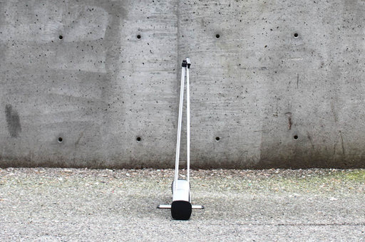 Rear view of an extra large table-top retractable banner stand displaying the silver aluminum base and vertical support pole set against a concrete wall.