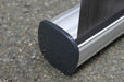 Close-up side view of the silver aluminum cassette base and dark gray plastic end cap of an extra-large tabletop retractable banner stand resting on pavement.