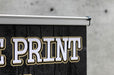 Close-up view of the top aluminum clamp rail and end clip securing the printed vinyl graphic on an extra-large tabletop retractable banner stand.