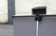 Close-up view of the black plastic top pole attachment clip securing the aluminum vertical support rod to the top rail of a tabletop banner stand.